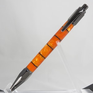 May include: A black and orange pen with a silver clip. The pen is on a clear acrylic stand.