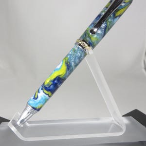 Bolígrafo estilo "Tritón" en resina acrílica multicolor brillante y con remolinos, con acabado cromado brillante y herrajes dorados. Mi artículo 105574.