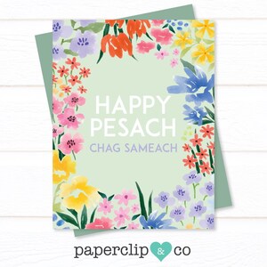 May include: A greeting card with a light green background and a floral border. The card reads "HAPPY PESACH CHAG SAMEACH" in white text. The floral border includes pink, yellow, orange, and blue flowers. The card is paired with a green envelope.