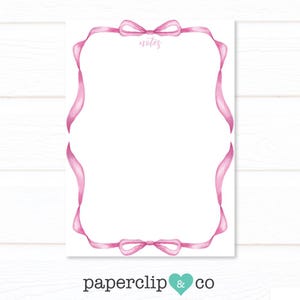 Può includere: Un foglio di carta da lettere stampabile con un bordo di nastro rosa e un fiocco in alto. La parola "notes" è scritta in corsivo nella parte superiore del foglio.
