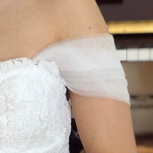 May include: A white off-the-shoulder wedding dress with a lace bodice and a tulle overlay on the shoulders.