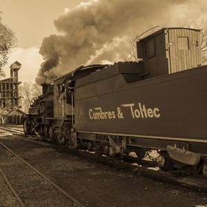 May include: A vintage steam locomotive with the words "Cumbres & Toltec" painted on the side, pulling a train of carriages. The locomotive is emitting smoke and steam, and the scene is in sepia tone.