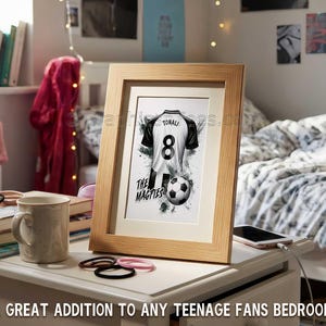 May include: Framed artwork featuring a black and white soccer jersey with the name "TONALI" and the number "8". A soccer ball is below the jersey. The text "THE MAGPIES" is also visible. The frame is light brown. The text at the bottom says "A GREAT ADDITION TO ANY TEENAGE FANS BEDROOM".