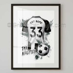 May include: Framed artwork featuring a black and white soccer jersey with the number 33 and the words "ANY NAME" above it. A soccer ball is positioned below the jersey, with the words "THE MAGPIES" beneath it. The background has a splash effect.