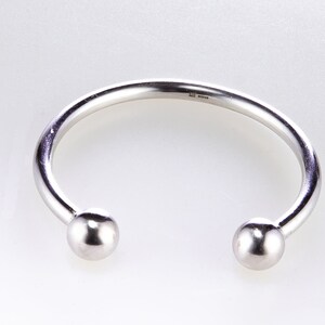 May include: A silver bangle bracelet with two round ends. The bracelet is made of a thick, smooth metal.