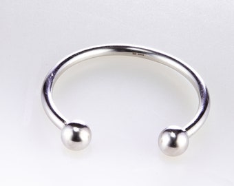 Op de afbeelding: Een zilveren armband met twee ronde uiteinden. De armband is gemaakt van dik, glad metaal.