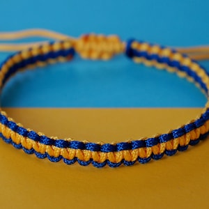 May include: A blue and yellow braided friendship bracelet. The bracelet is made with two strands of cord, one blue and one yellow, that are woven together in a simple pattern.