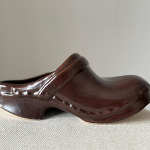 May include: A brown ceramic clog-shaped planter with a textured surface and a raised rim.