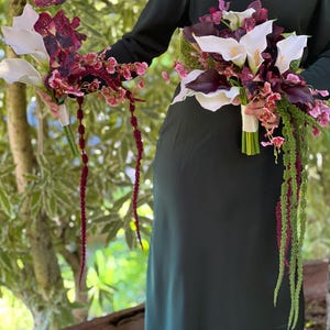 May include: Two floral bouquets featuring white calla lilies, deep purple orchids, and cascading amaranth stems. The bouquets are wrapped in white ribbon at the stems. The arrangement includes a mix of dark burgundy and white floral elements.
