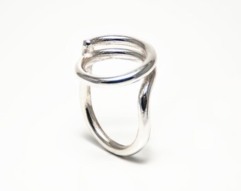 May include: A silver ring with a twisted, open design. The ring is made of a single piece of metal that is bent and twisted to create the unique shape.