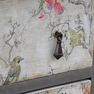 May include: A vintage-style dresser with two drawers, featuring a floral and bird design. The top drawer has a black metal knob and the text "Willow & Hobbs" is printed on the top.