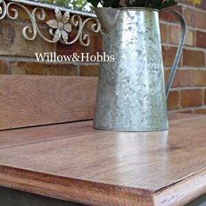 May include: A rustic wooden table top with a distressed gray finish. A galvanized metal pitcher with a floral design and the word "Lavender" is sitting on the table. The pitcher is filled with yellow flowers.