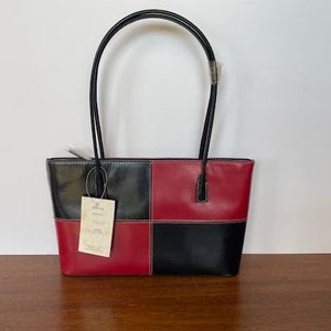 Puede incluir: Un bolso tote de cuero negro y rojo con un patrón de cuadros. El bolso tiene dos asas superiores y una pequeña etiqueta adjunta en la parte delantera.
