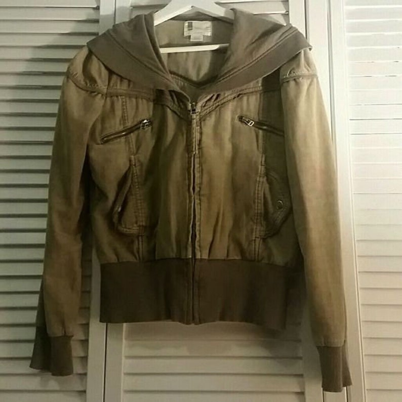 May include: A khaki green hooded jacket with a zipper closure and multiple pockets. The jacket has a ribbed waistband and cuffs.