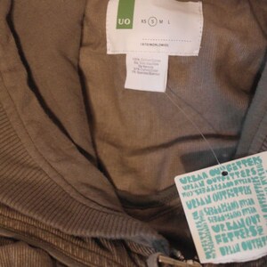 May include: A brown corduroy hoodie with a zipper closure and a tag that reads "Urban Outfitters". The tag is white with teal blue text. The hoodie has a ribbed collar and a size tag that reads "XS S M L".