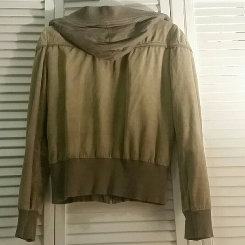 May include: A beige hooded jacket with a zipper closure. The jacket has a ribbed waistband and cuffs.