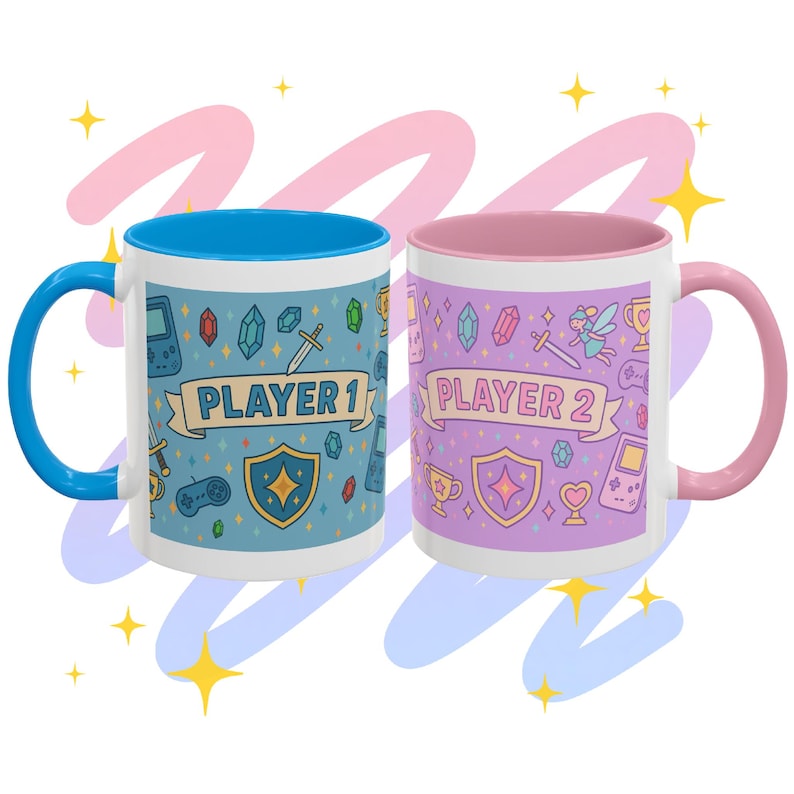 Op de afbeelding: Twee witte keramische mokken met gaming-thema's. E&eacute;n mok heeft een blauwe handgreep en binnenkant, de andere heeft een roze handgreep en binnenkant. Elke mok heeft een banner met "PLAYER 1" en "PLAYER 2" en game-gerelateerde graphics.