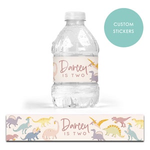 May include: Water bottle label with a pink dinosaur theme. The label says "Darcey is Two" and features colorful dinosaurs.
