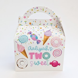 May include: A white cardboard gable box featuring a colorful pattern of ice cream cones, donuts, lollipops, and candies. The front displays the text Aaliyah's TWO sweet in blue and pink lettering, with a sprinkle design on the handle and top panels.