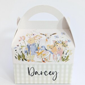 Könnte beinhalten: Eine hellgrüne und weiß karierte Geschenkbox mit Griff. Die Box zeigt eine Aquarellillustration eines Kaninchens, einer Ente, eines Schweins und einer Ziege in einem Blumenfeld. Der Name "Darcey" steht auf der Vorderseite.