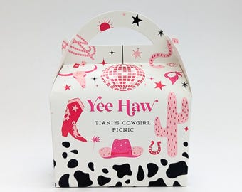 Puede incluir: Caja de regalo blanca con asa, con ilustraciones rosas con temática de vaquera. La caja incluye una bota de vaquero, un cactus y una bola de discoteca. El texto en la caja dice "Yee Haw" y "TIANI'S COWGIRL PICNIC". La parte inferior tiene un estampado de vaca en blanco y negro.
