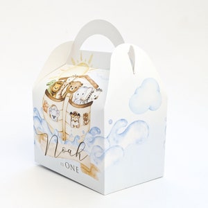 May include: A white party favor box with a handle, featuring an illustration of Noah's Ark with animals. The box has a watercolour design of blue waves, clouds, and a sun. The text "Noah is One" is displayed on the front.