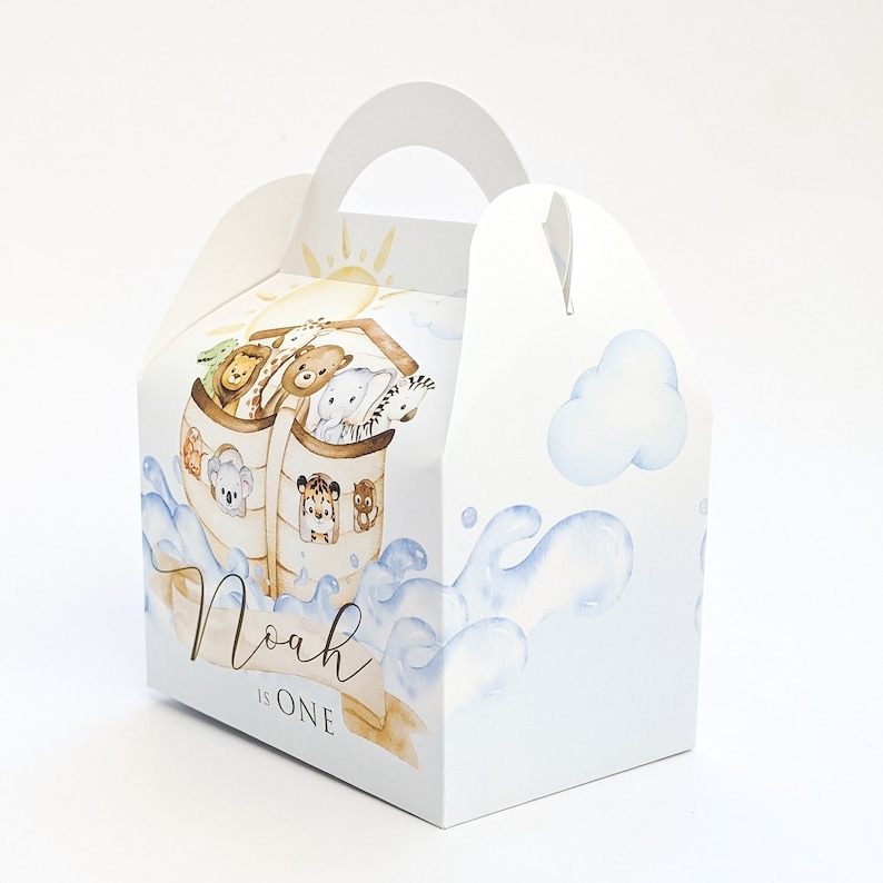 May include: A white party favor box with a handle, featuring an illustration of Noah's Ark with animals. The box has a watercolour design of blue waves, clouds, and a sun. The text "Noah is One" is displayed on the front.