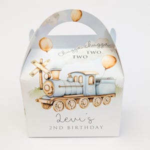Puede incluir: Caja de regalo azul claro con temática de tren, con asa, que presenta una ilustración de acuarela de un tren, globos y una señal de cruce de ferrocarril. También se ve el texto "Chugga Chugga Two Two" y "2nd Birthday de Levi".