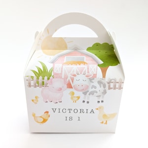 Könnte beinhalten: Eine weiße Geschenkbox mit Henkel, die eine Farm-Szene mit einem roten Stall, einer Kuh, einem Schwein und Küken zeigt. Die Box ist mit grünem Gras und einer gelben Sonne verziert. Der Text "VICTORIA IS 1" ist auf der Vorderseite der Box gedruckt.
