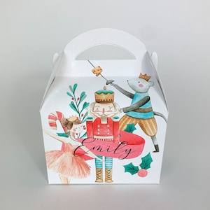 Può includere: Scatola regalo bianca con manico, con un'illustrazione ad acquerello di una scena dello Schiaccianoci. Il design include un soldato Schiaccianoci, un topo, una ballerina e il nome "Emily" in corsivo. Tema festivo.