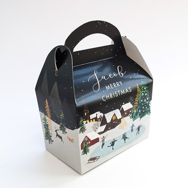 May include: A festive gift box with a winter village scene. The box features a black background with the name "Jacob" and "MERRY CHRISTMAS" in white script. The box has a handle and a snowy landscape with skaters.