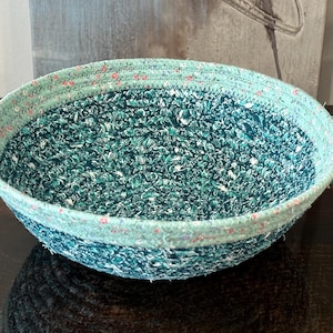 May include: A white ceramic mug with a black handle and the text "But First, Coffee" in a bold, black font. The mug is sitting on a wooden surface. The mug appears to be 12 ounces.