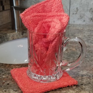 May include: A clear glass mug with a handle, filled with a coral-colored towel. The mug is sitting on a coral-colored towel coaster.