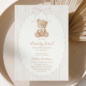 May include: A baby shower invitation with a teddy bear illustration. The invitation features the text "Bearly Wait" and event details. The design is in soft beige tones with a scalloped border. The invitation is on a beige plate.