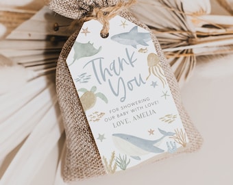 May include: A small burlap bag tied with twine, holding a gift tag. The tag features watercolor illustrations of sea creatures like a whale, shark, and jellyfish, with the words "Thank You" and a personalized message. The overall theme is a baby shower.