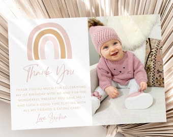 May include: A pink and gold rainbow with the text "Thank You" and a message thanking guests for celebrating a first birthday. The message includes the name "Sophia". A photo of a baby girl wearing a pink sweater and hat is in the corner of the card.
