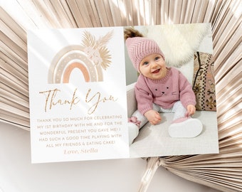 May include: A thank you card with a rainbow and floral design. The card has the text "Thank You" in gold glitter lettering and a message thanking guests for celebrating the child's first birthday. The card also includes a photo of a baby girl wearing a pink sweater and a pink hat.