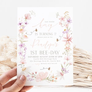 K&ouml;nnte beinhalten: Eine Einladung zu einer ersten Geburtstagsfeier f&uuml;r Penelope im Blumendesign. Die Einladung zeigt einen Kranz aus rosa und lila Blumen mit Bienen und dem Text "Unser kleines Honigbienenkind wird 1! Bitte feiern Sie mit uns Penelope's 1. Bienentag. Samstag, 25. August um 14:00 Uhr. Castle Hill Heritage Park. 22z Heritage Park Dr. Castle Hill. RSVP Michelle 0412 345 678"