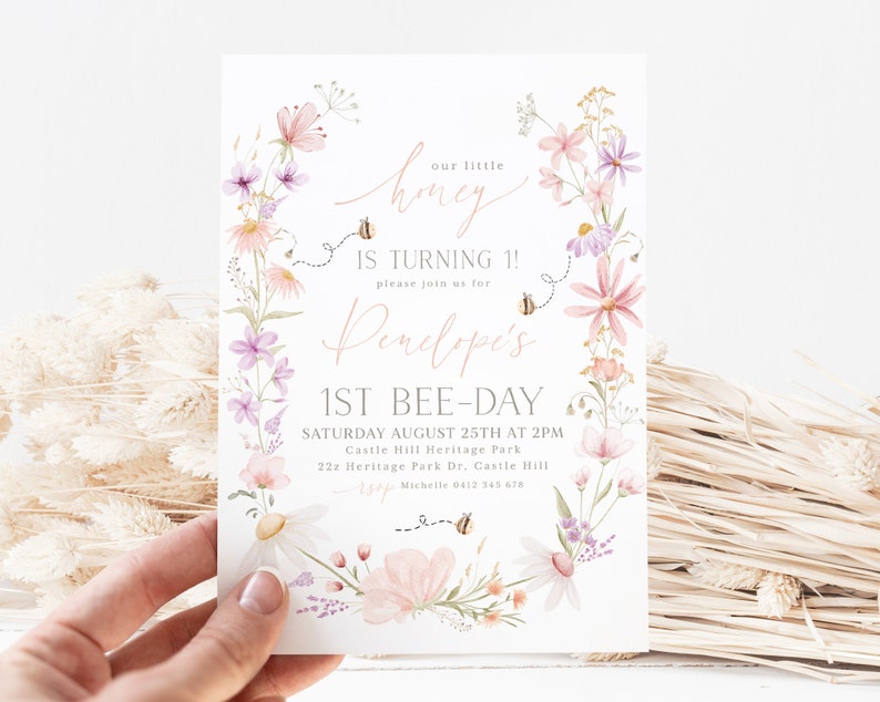 K&ouml;nnte beinhalten: Eine Einladung zu einer ersten Geburtstagsfeier f&uuml;r Penelope im Blumendesign. Die Einladung zeigt einen Kranz aus rosa und lila Blumen mit Bienen und dem Text "Unser kleines Honigbienenkind wird 1! Bitte feiern Sie mit uns Penelope's 1. Bienentag. Samstag, 25. August um 14:00 Uhr. Castle Hill Heritage Park. 22z Heritage Park Dr. Castle Hill. RSVP Michelle 0412 345 678"