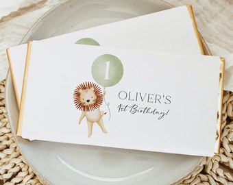 May include: Two white chocolate bar wrappers with gold foil accents. The wrapper features a cartoon lion holding a green balloon with the number "1" on it. The text "Oliver's 1st Birthday!" is printed on the wrapper.