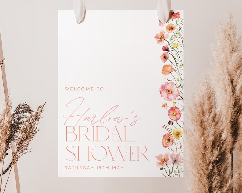 Pu&ograve; includere: Un cartello bianco con testo rosa che dice "Benvenuti al Bridal Shower di Harlow Sabato 15 maggio". Il cartello ha un bordo floreale con fiori rosa e arancioni.
