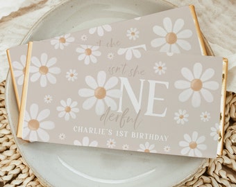 May include: A light brown chocolate bar wrapper with a white daisy pattern. The text "Isn't she one derful" and "Charlie's 1st Birthday" is printed on the wrapper.