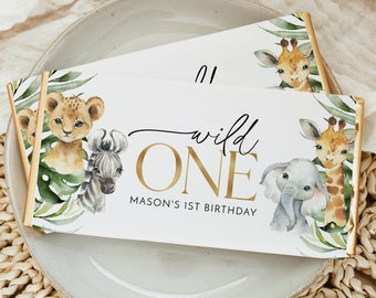 May include: White and gold 'Wild One' party favor with a jungle animal theme. The favor features a lion, zebra, elephant, and giraffe with green leaves and gold accents. The text reads 'Wild One' with 'Mason's 1st Birthday' below.