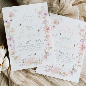 K&ouml;nnte beinhalten: Zwei florale Einladungen zu einem 1. Geburtstag. Die Einladungen sind wei&szlig; mit rosa und lila Blumen und Bienen. Der Text auf den Einladungen lautet "Unser kleiner Honig wird 1! Bitte feiern Sie mit uns Penelopes 1. Bienentag." Die Einladungen enthalten auch das Datum, die Uhrzeit und den Ort der Party.
