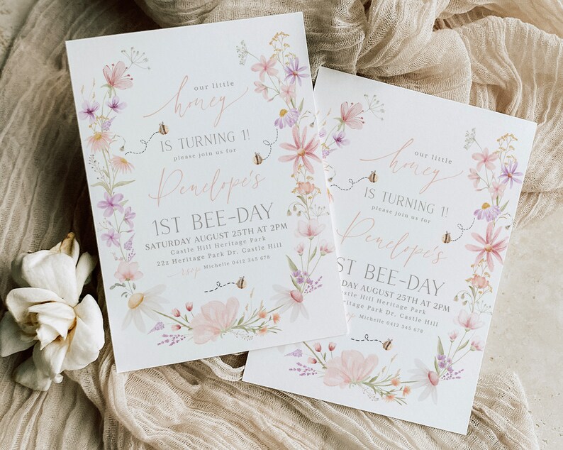 K&ouml;nnte beinhalten: Zwei florale Einladungen zu einem 1. Geburtstag. Die Einladungen sind wei&szlig; mit rosa und lila Blumen und Bienen. Der Text auf den Einladungen lautet "Unser kleiner Honig wird 1! Bitte feiern Sie mit uns Penelopes 1. Bienentag." Die Einladungen enthalten auch das Datum, die Uhrzeit und den Ort der Party.