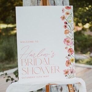 Pu&ograve; includere: Un cartello di benvenuto bianco con accenti floreali rosa e il testo "Benvenuti al Bridal Shower di Harlow, sabato 15 maggio".