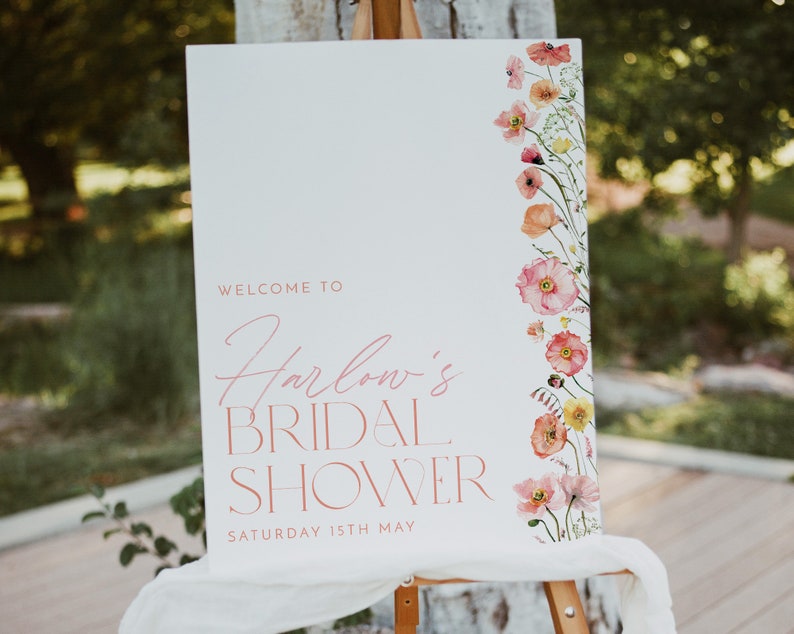 Pu&ograve; includere: Un cartello di benvenuto bianco con accenti floreali rosa e il testo "Benvenuti al Bridal Shower di Harlow, sabato 15 maggio".