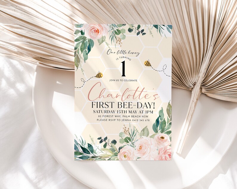 May include: An invitation card with a floral design and the text "Charlotte's First Bee-Day!" features a honeycomb background, watercolor roses, and greenery. The design includes a bee graphic and the words "Our little honey is turning 1."