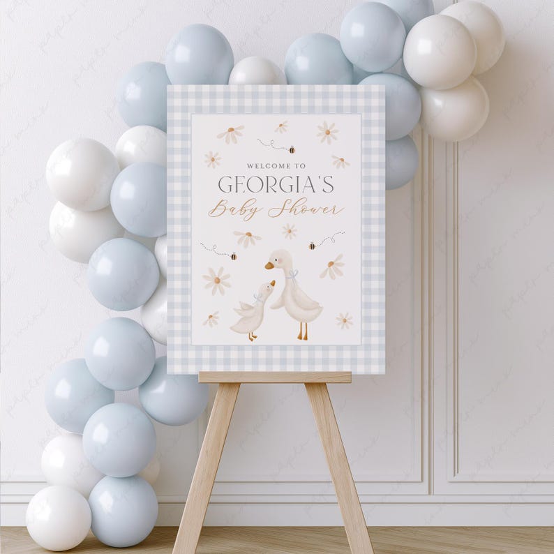K&ouml;nnte beinhalten: Ein Willkommens-Schild f&uuml;r eine Babyparty mit einem blau-wei&szlig; karierten Hintergrund. Das Schild zeigt zwei wei&szlig;e G&auml;nse mit braunen Augen und Schn&auml;beln und den Text "Willkommen zur Babyparty von Georgia".