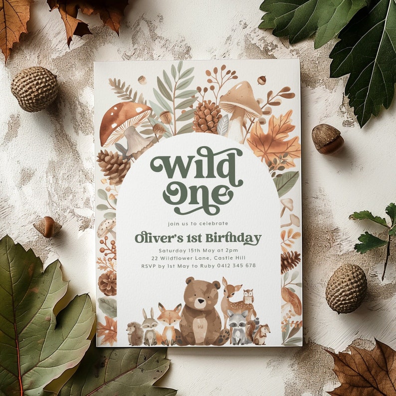 May include: A woodland-themed first birthday invitation with a green and brown "Wild One" title. The invitation features a watercolor illustration of forest animals, including a bear, fox, deer, and raccoon, surrounded by leaves, mushrooms, and pine cones.